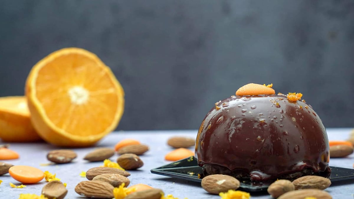 A dark chocolate dessert with candied orange peel, half an orange and almonds