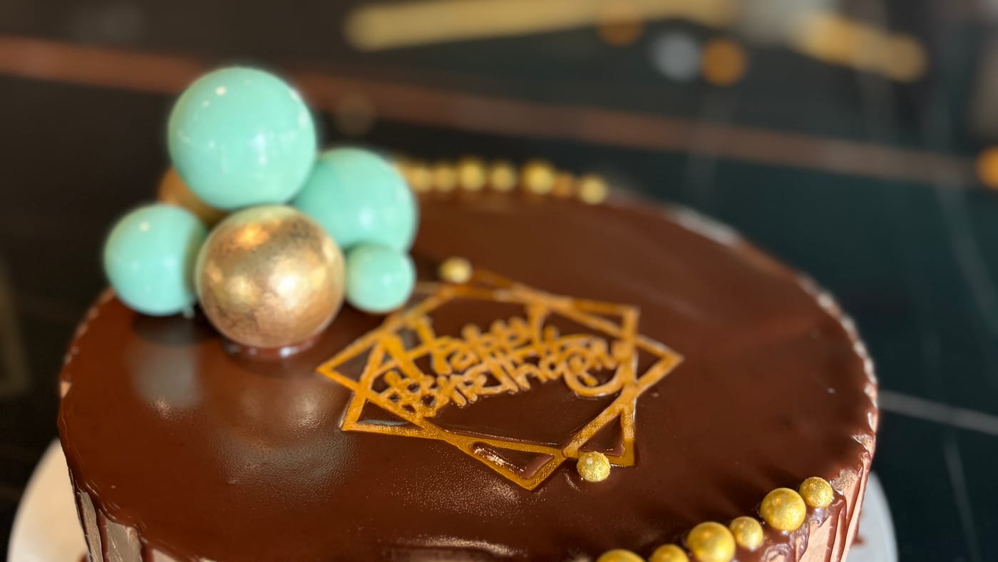 A cake with chocolate glaze, gold pearls and turquoise spheres, on a black marble counter