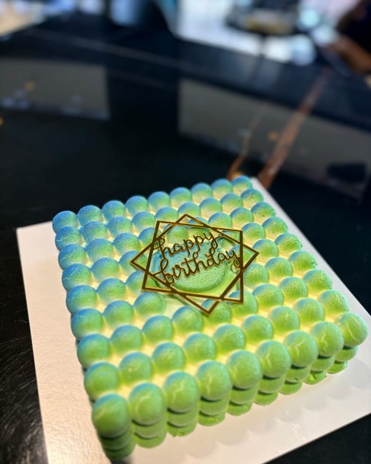 A green cake with a bubble-piped surface and gold lettering, on a white board