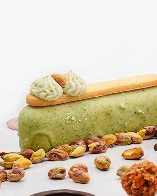 Kolač od pistaća sa hrskavom korom i rozetama od kreme, sa celim pistaćima oko njega