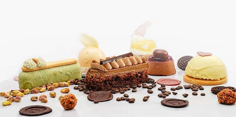 A row of Hannes cakes and gelato on a white ground, with coffee beans and pistachios